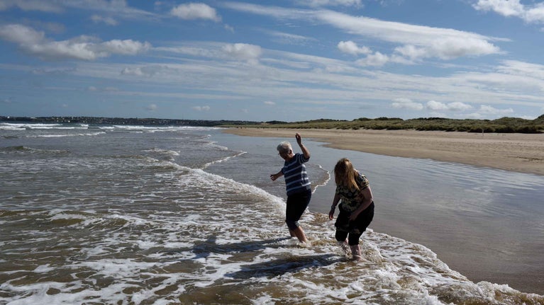 Two visitors paddling in the water on the beach at Portstewart Strand, County Londonderry, Northern Ireland.